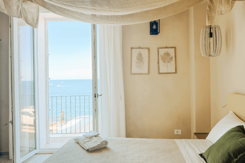 Sea view suite Palazzo Russo Ortigia, the balcony opens up to the sea view, the blanket is light-colored, the walls are beige